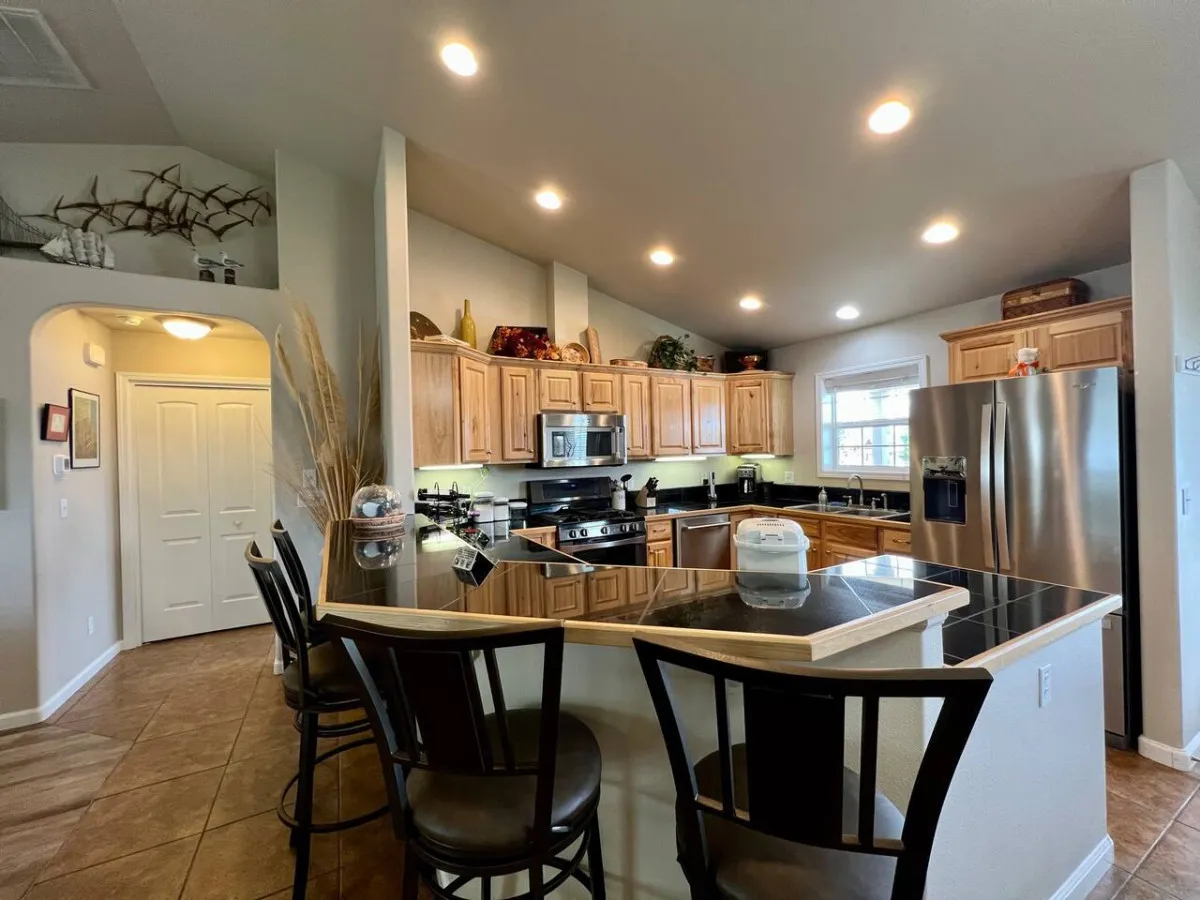 This image features an inviting kitchen island with bar stools, complemented by stainless steel appliances and warm wooden cabinetry. The space is designed for both cooking and casual dining, with upgraded finishes that reflect elegance and functionality.