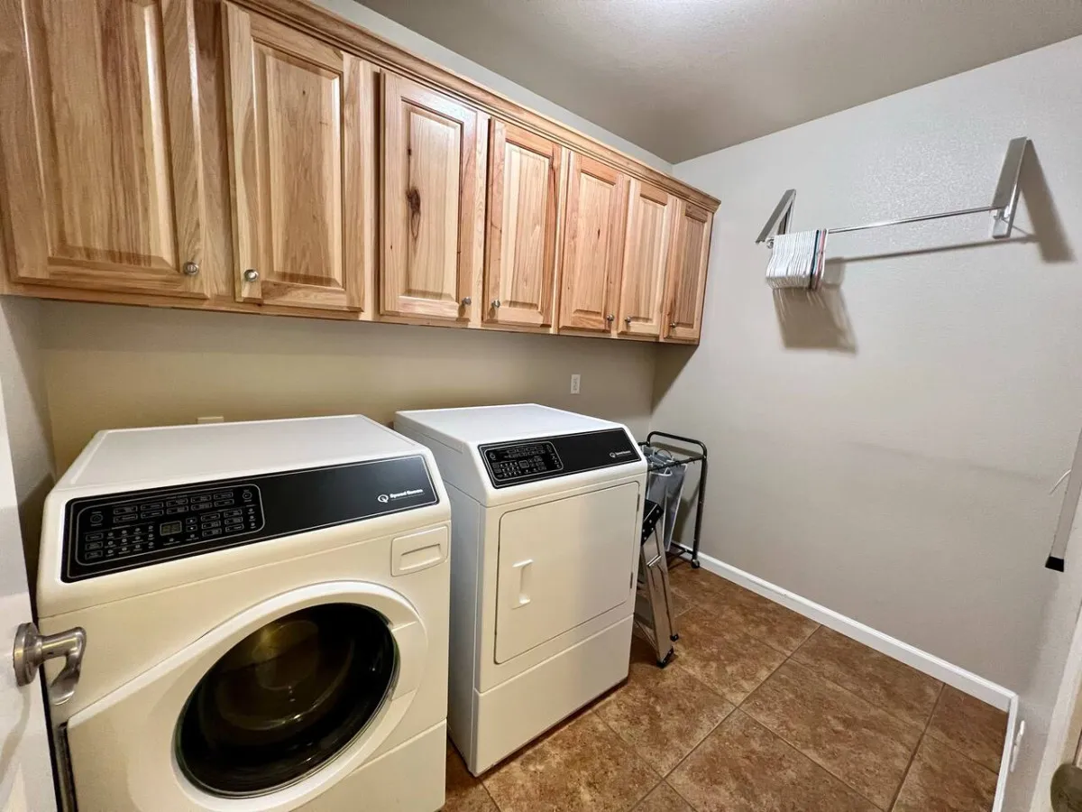 This image presents a bright, practical laundry room featuring a washing machine, dryer, and wooden cabinets for storage. The space feels orderly and purposeful, highlighting its capacity for family laundry routines and organizational ease.