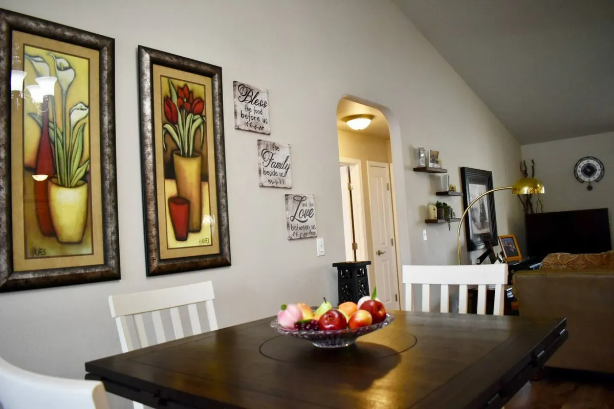 This image captures the dining area, featuring a welcoming dining table adorned with a fruit bowl, tasteful wall art, and a doorway leading to adjacent spaces. The setting feels intimate yet functional, ready for shared meals or special occasions.