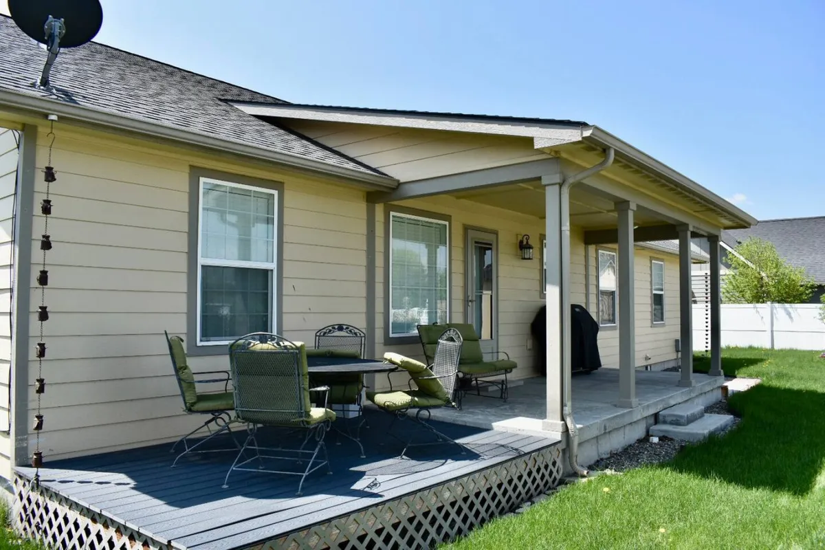This image features a relaxed and inviting backyard setting with patio furniture, a grill, and a green lawn. The covered patio area creates an ideal spot for outdoor dining and comfortable lounging, while the greenery amplifies the sense of privacy and tranquility.