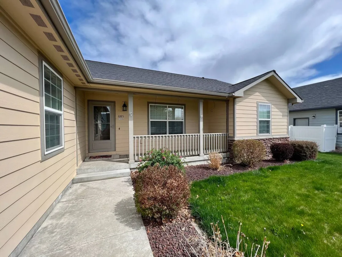 An exterior view of the home showcasing the front porch, landscaped garden, and entryway. The green surroundings and open porch invite guests to enjoy the outdoors, mirroring the retreat's accessibility to historic downtown and local attractions.