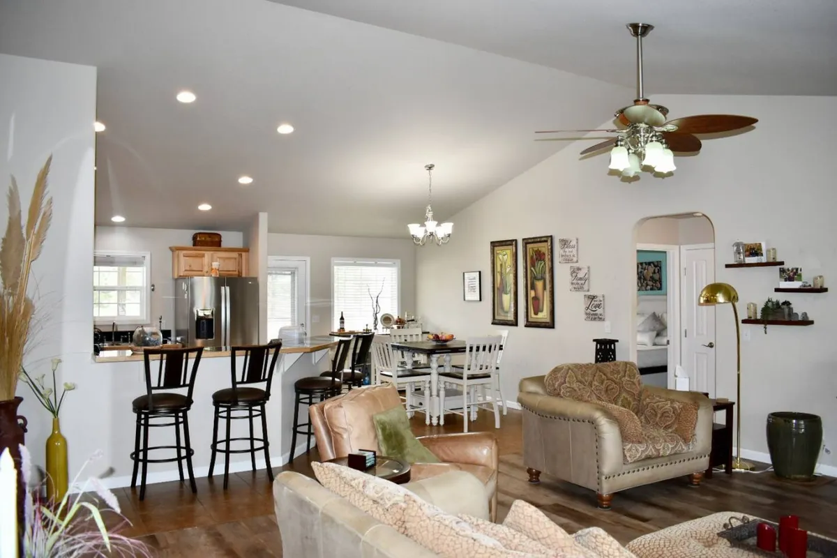 The photo showcases a cohesive open-plan space where a comfortable seating area with a couch and armchairs flows effortlessly into a dining table and a visible kitchen counter with bar stools. Decorative wall art ties the design together, creating a space for relaxing, dining, and conversation.