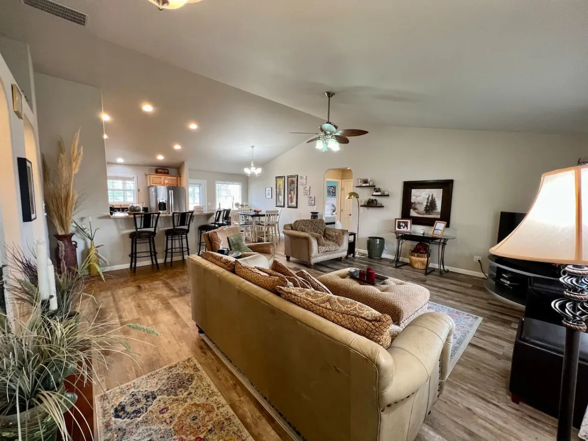 The image showcases a warm, inviting living and dining space featuring a plush sofa, comfortable chairs, an elegant dining area set for gatherings, tasteful artwork on the walls, and a softly glowing lamp creating a cozy ambiance. The layout is open and perfect for socializing, with ample natural light and stylish décor that feels both welcoming and refined.