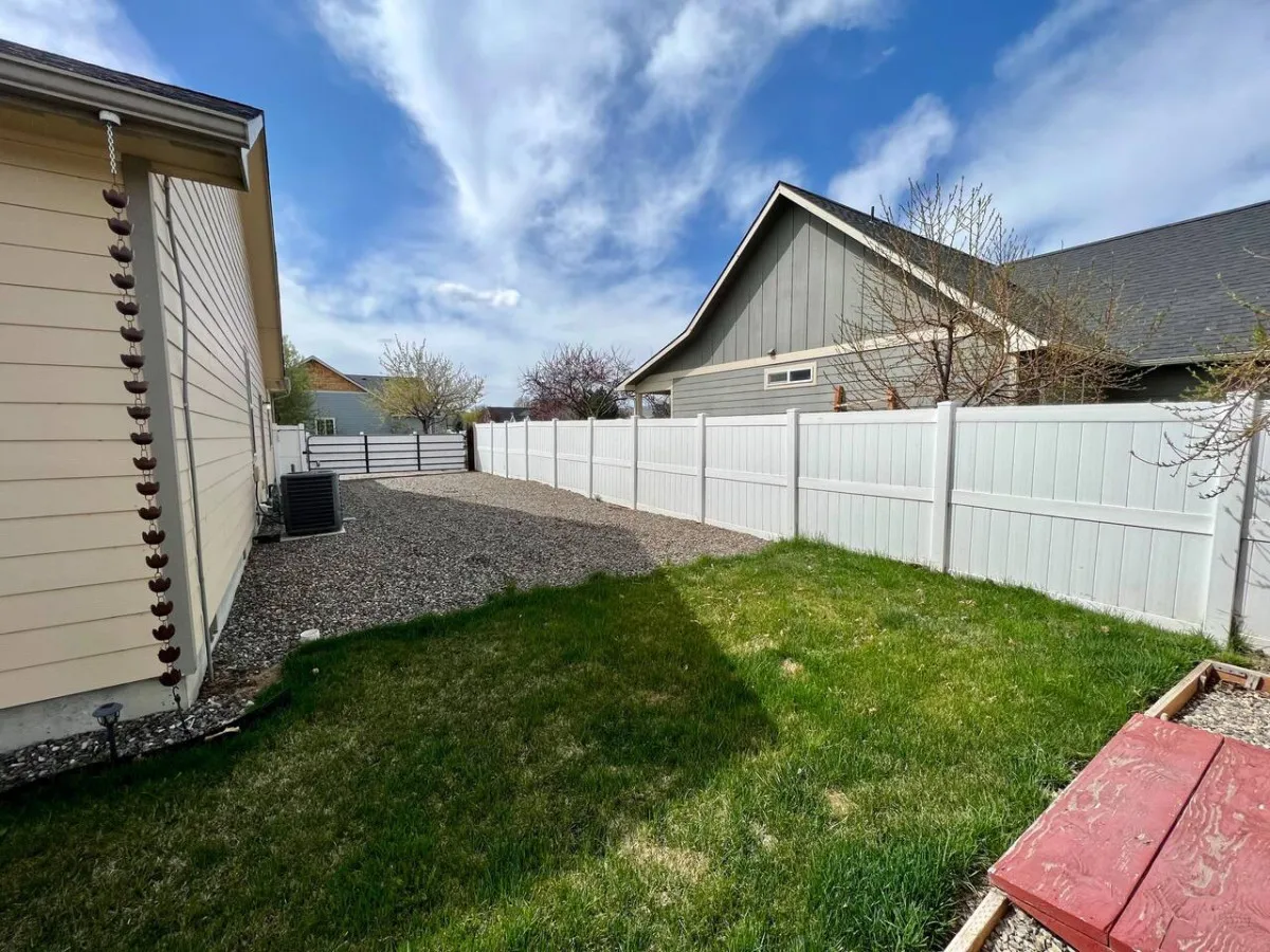 The exterior of Sweet Retreat features a peaceful grassy area bordered by a white fence and a gravel pathway. The outdoor space is inviting for morning coffee, relaxation, or winding down after exploring town.