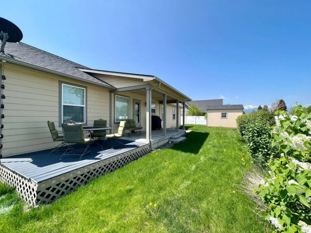 A patio seating area overlooks a grassy lawn and the exterior of the home, offering ample space for outdoor dining or simply relaxing in a serene garden setting. The area is bathed in soft, natural light, suggesting a peaceful, private outdoor retreat.